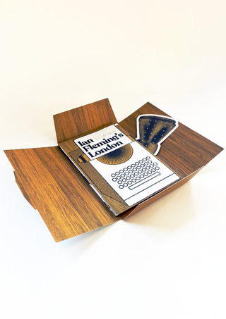 Open wood-effect packaging for Ian Fleming's London lying flat, showing the inner typewriter-illustrated cover and the bow tie-shaped card, which carries a Vesper cocktail recipe on its reverse.